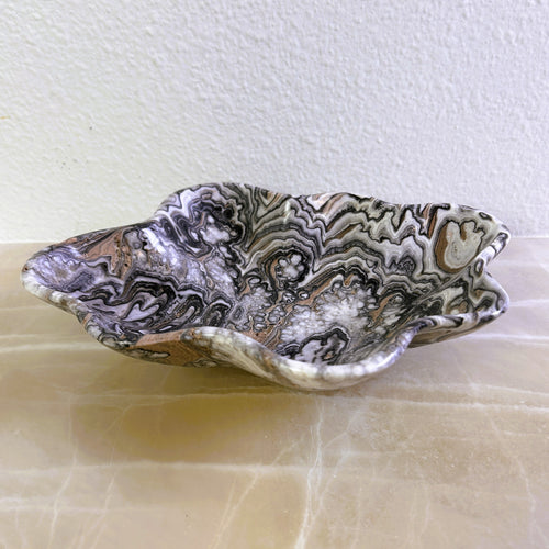 An elegant hand-carved bowl with capricious veins in beige, light brown, and dark brown tones, placed on a marble surface.